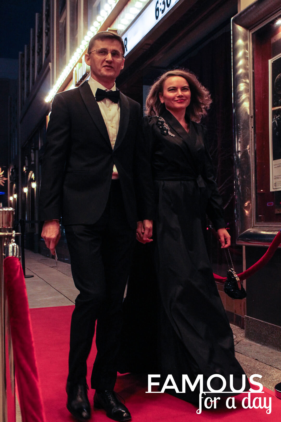 Well-dressed couple walking together down a red carpet at night outside a theater marquee